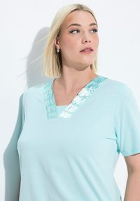 Camiseta de color azul claro con mangas cortas, que presenta un escote en V adornado con una tela texturizada de brillo contrastante. Material suave y liso.