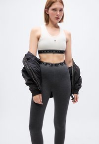 Λευκό αθλητικό μπουστάκι με μικρό τρίγωνο λογότυπο, μαύροι κολάν ψηλόμεσοι με λωρίδα "TOMMY JEANS" και μαύρο μπουφάν bomber. Λείος υφισμός.