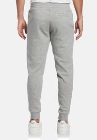 Grijze joggingbroek met een taps toelopende pasvorm, elastische tailleband en een achterzak, gecombineerd met witte sneakers met minimale branding.
