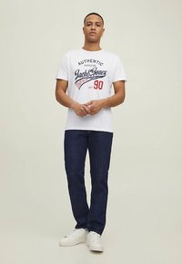 White t-shirt with "Jack & Jones" graphic in blue and red, paired with dark blue jeans and white sneakers. Simple, casual design.