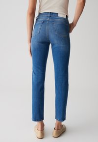 Jeans in denim blu chiaro con taglio dritto, cinque tasche e finitura sbiadita. Indossati con scarpe beige senza lacci.