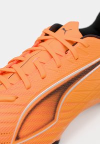 Scarpa da calcio arancione brillante con superficie testurizzata, accenti neri e dettagli argentati riflettenti lungo il lato e i lacci.