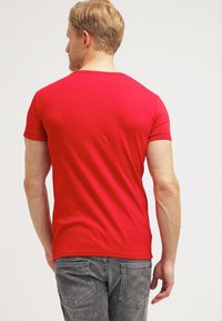 Kurzes rotes T-Shirt aus glattem Stoff mit Rundhalsausschnitt. Getragen mit grauen Denim-Jeans, die über Taschendetails verfügen.