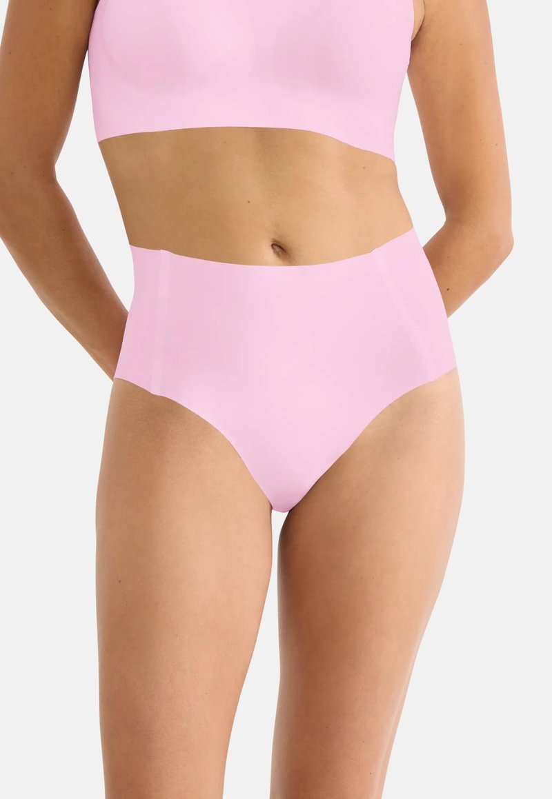 Γυναίκα που φοράει αδιάκοπα παστέλ ροζ εσώρουχα με ψηλή μέση και ταιριαστό κοντό τοπ, πάνω σε απλό λευκό φόντο.