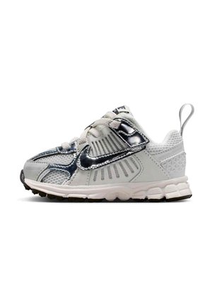 Baskets pour tout-petits blanches et argentées avec panneaux en mesh, languette au talon, semelle épaisse et swoosh Nike noir brillant sur le côté.