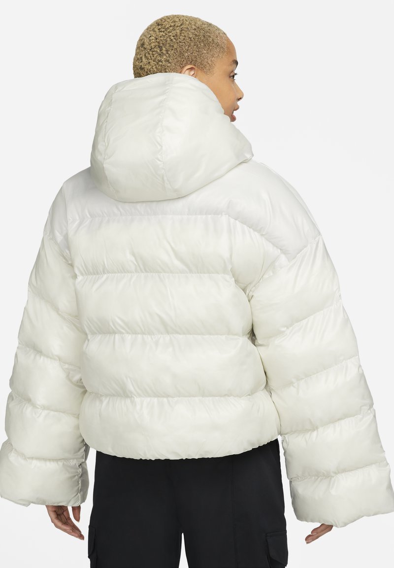 Chaqueta puffer blanca con capucha, que presenta un diseño acolchado, mangas anchas y un corte corto. Acabado liso y brillante con una textura suave.