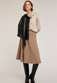 Blusa di seta beige, giacca di pelle nera e una gonna color cammello al ginocchio. Stivali alti neri con motivo coccodrillo. Design semplice e aderente.