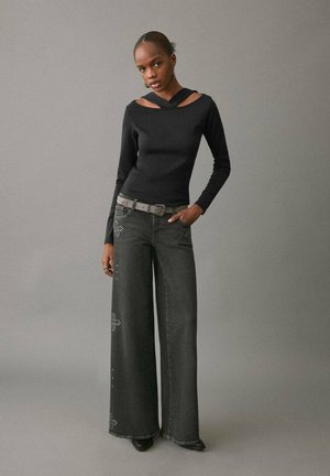 Top negru cu mâneci lungi, decolteu încrucișat și detalii decupate, asortat cu blugi din denim închis cu croială largă și accente cu ținte.