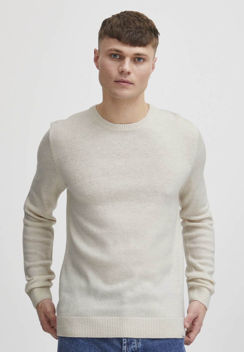 Pull en maille couleur crème avec un col rond, des manches longues et des poignets et un ourlet côtelés. Texture douce avec un motif subtil.