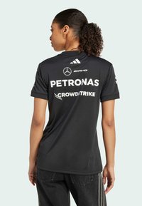 Crni sportski dres prikazan sa stražnje strane s bijelim logotipima za Petronas, CrowdStrike i Mercedes-AMG. Kratki rukavi i tkanina koja odvlači vlagu.