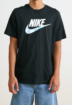 Osoba nosząca czarną koszulkę Nike z białym logo i niebieskim wzorzystym symbolem Swoosh, w połączeniu z jasnoniebieskimi jeansowymi szortami.