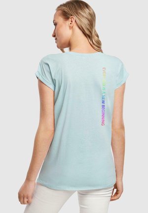 Hellblaue Kurzarm-T-Shirts mit aufgerollten Ärmeln, auf dem Rücken befindet sich ein vertikaler Regenbogen-Textdruck mit der Aufschrift "JEDER TAG IST EIN NEUER BEGINN."