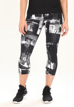 Czarno-białe legginsy capri z geometrycznym wzorem, z różnymi teksturami i kropkami, w połączeniu z czarnymi butami sportowymi.