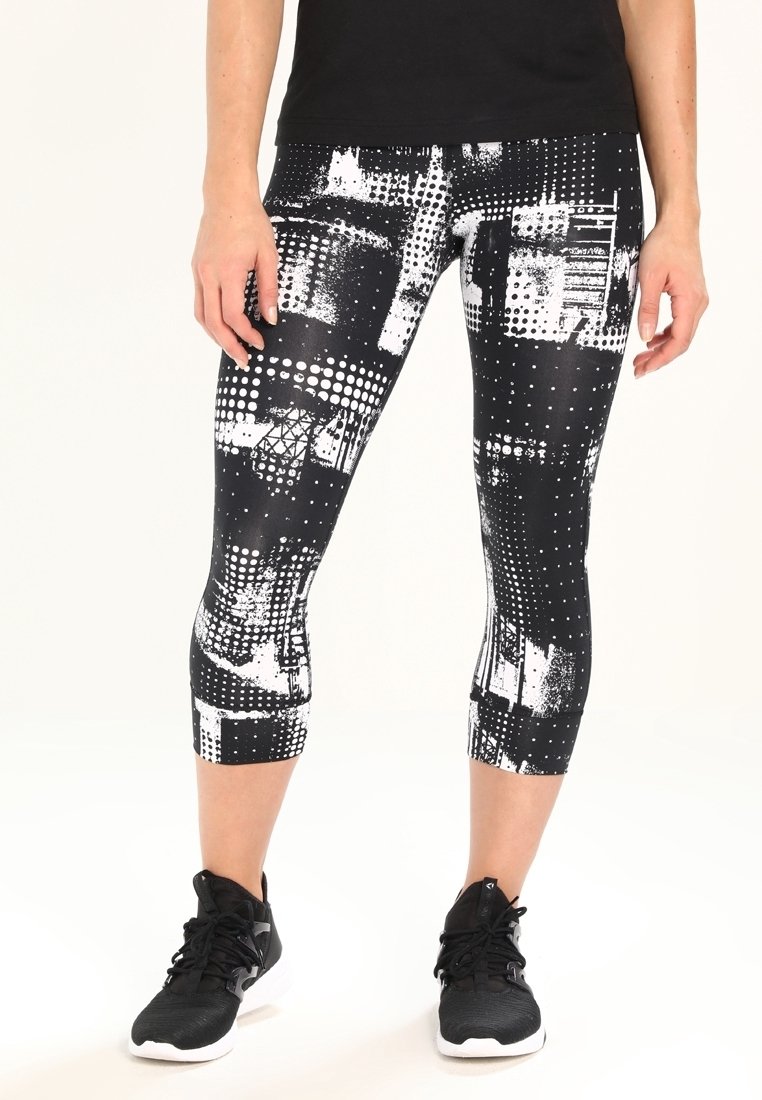 Černo-bílé capri legíny s geometrickým vzorem, obsahující různé textury a puntíky, spárovány s černými sportovními botami.