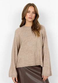 Beige, mjukstickad tröja med rundad halsringning, raglanärmar och ribbad nederkant, tillsammans med en brun fusk läderkjol.