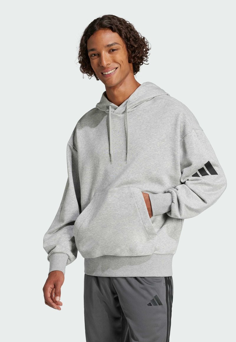 Felpa grigia con cappuccio, tasca a marsupio, vestibilità rilassata e dettagli neri del logo Adidas sulle maniche. Tessuto morbido e con texture.