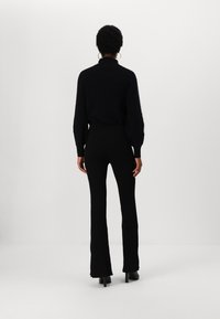 Top lung cu mânecă lungă, din tricot negru cu textură ribbed, asortat cu pantaloni evazați cu talie înaltă, având o textură netedă și manșete subtile, completat cu cizme cu toc.