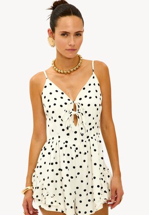 Robe courte à pois blancs avec un décolleté en V plongeant, un lien à l'avant et des ourlets volants. Fines bretelles et motif de pois ludique sur l'ensemble.