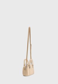 Kleine beige handtas met twee bovenhandvatten en een lange verstelbare schouderriem, weergegeven op een effen lichtgrijze achtergrond.
