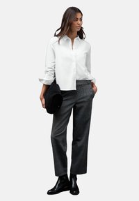 Chemise blanche à boutons, pantalon gris à carreaux, bottines noires à talons, et un sac noir. Présente une coupe décontractée et des manches retroussées.