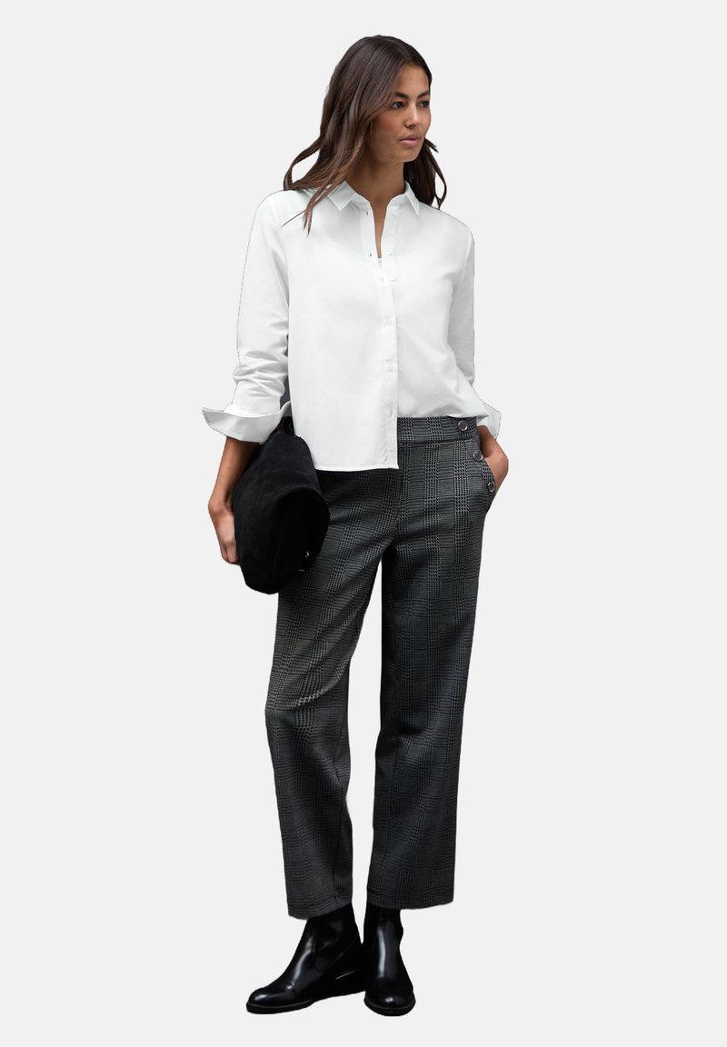 Chemise blanche à boutons, pantalon gris à carreaux, bottines noires à talons, et un sac noir. Présente une coupe décontractée et des manches retroussées.