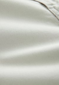 Gros plan sur un tissu lisse de couleur claire avec des coutures visibles le long du bord.