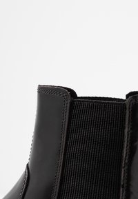 Czarne botki za kostkę z błyszczącej lakierowanej skóry, elastycznym panelem bocznym i kontrastowym szwem. Gładka tekstura z czystym, minimalistycznym designem.