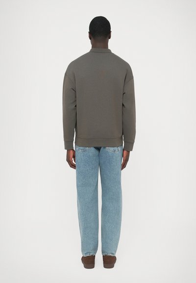 Καφέ πουλόβερ με γιακά, άνετη εφαρμογή και ριμπ μανσέτες, σε συνδυασμό με ανοιχτόχρωμα τζιν με ίσια γραμμή και καφέ παπούτσια. Απλός, μινιμαλιστικός σχεδιασμός.