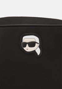 Borsa nera in nylon con un emblema di gomma prominente raffigurante una testa con un codino bianco e occhiali neri sul davanti.