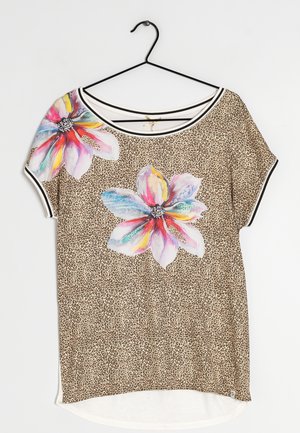 Top met korte mouwen in luipaardprint en grote, kleurrijke bloemmotieven, ronde halslijn met zwart-witte bies, hangend aan een zwarte hanger.