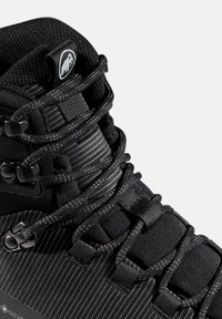 Primer plano de una bota de senderismo negra con cordones redondos, que presenta una lengüeta acolchada y un logo blanco de mamut en la etiqueta superior.