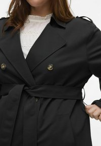 Czarny podwójnie zapięty płaszcz trencz z paskiem w talii, szerokimi klapami i guzikami. Materiał gładki, o dobrze dopasowanym kroju i dwóch bocznych kieszeniach.