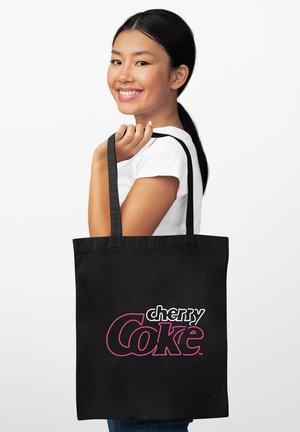 Borsa tote nera con la scritta "cherry Coke" in rosa e bianco. La borsa ha robuste spalline e un design semplice e rettangolare.