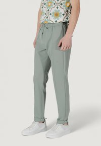 Pantaloni a tubo verde chiaro con vita elasticizzata e tasche laterali, abbinati a sneaker bianche. Tessuto morbido con dettagli a pieghe.