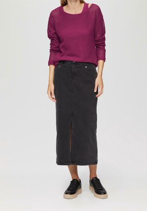 Frau trägt ein lila langärmeliges Mesh-Top, schwarzen hoch taillierten Midirock mit Frontschlitz und schwarze Plateausneaker, steht vor einfachem Hintergrund.