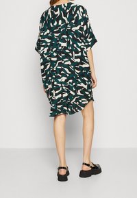 Sukienka z krótkim rękawem w czarnym, morskim i kremowym abstrakcyjnym wzorze. Luźny materiał, lekko zaokrąglony dół, zestawiona z czarnymi sandałami na platformie.