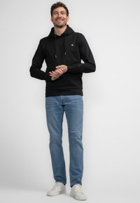 Sudadera negra con capucha y cordones, combinada con jeans de mezclilla azul claros y zapatillas blancas. Textura suave, diseño simple, sin patrones visibles.