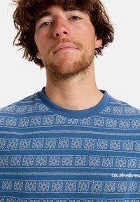 Blue short-sleeve t-shirt with a circular neckline, featuring white geometric patterns and a white logo on the left side.