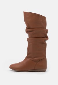 Bottes décontractées en cuir marron avec un bout rond et un talon bas, présentant une surface douce et texturée ainsi qu'une coupe ample pour le confort.