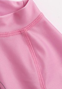 Ljust rosa tyg med en slät textur, med hög hals och synlig sömnad längs sömmarna.