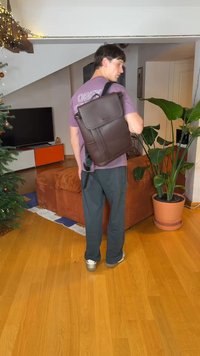 Brun læder messenger-taske med klap, enkelt skulderrem og forlommer. Modellen har afslappet tøj på og står i en stue.