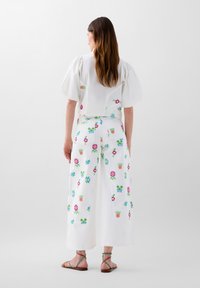 Witte top met pofmouwen en wijde broek met kleurrijke bloemenborduursels. Sandalen met dunne, multikleurige banden. Glad katoen textuur.