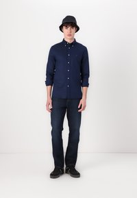 Cămash navy cu mâneci lungi, asortat cu blugi negri din denim și o pălărie bucket neagră. Adidașii negri completează ținuta.