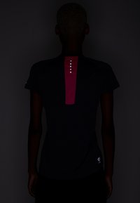 Camiseta atlética negra de manga corta, con un panel rosa y cinco botones blancos en la parte posterior, fabricada con un tejido suave y ligero.