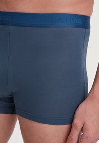 Marineblauwe boxershorts met een gladde textuur en een zachte tailleband met de merknaam "CALIDA" erop gedrukt.