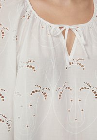 Weiße Baumwollbluse mit gerafftem Ausschnitt, Bindeband und aufwendigen gestickten Blumenmustern mit Ausschnittakzenten.