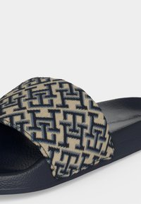 Sandale à glissière avec semelle texturée bleu marine et bride en tissu beige ornée d'un motif géométrique bleu marine répétitif.