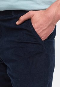 Mörkblå kordflortbyxor med en strukturerad yta. Har en sidoficka, avslappnad passform och kontrasterande sömmar längs kanterna.
