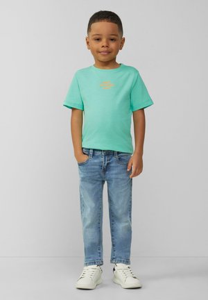 Miętowa koszulka z krótkim rękawem z pomarańczowym tekstem graficznym, zestawiona z jasnoniebieskimi dżinsami i białymi sneakerami. Czysty, prosty design.