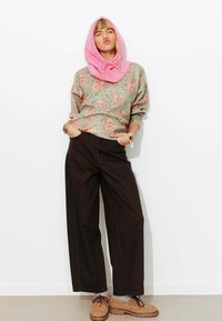 Pull en maille à motif floral vert et rose, associé à un pantalon large noir et des chaussures beige. Capuche rose avec cordon de serrage.